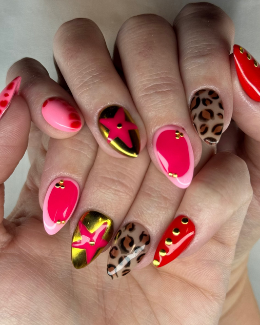 A bold luxe set featuring hot pink gloss, gold chrome accents, leopard print details, and studded statement nails.